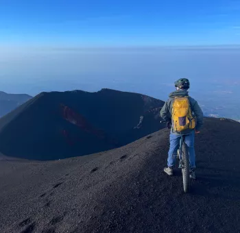 Cycliste en VTT électrique sur les coulées de lave de l'Etna face aux cratères sommitaux fumants